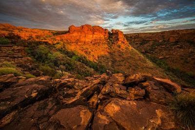 Red sandstone cliffs lit by low sun above a boulder strewn gorge